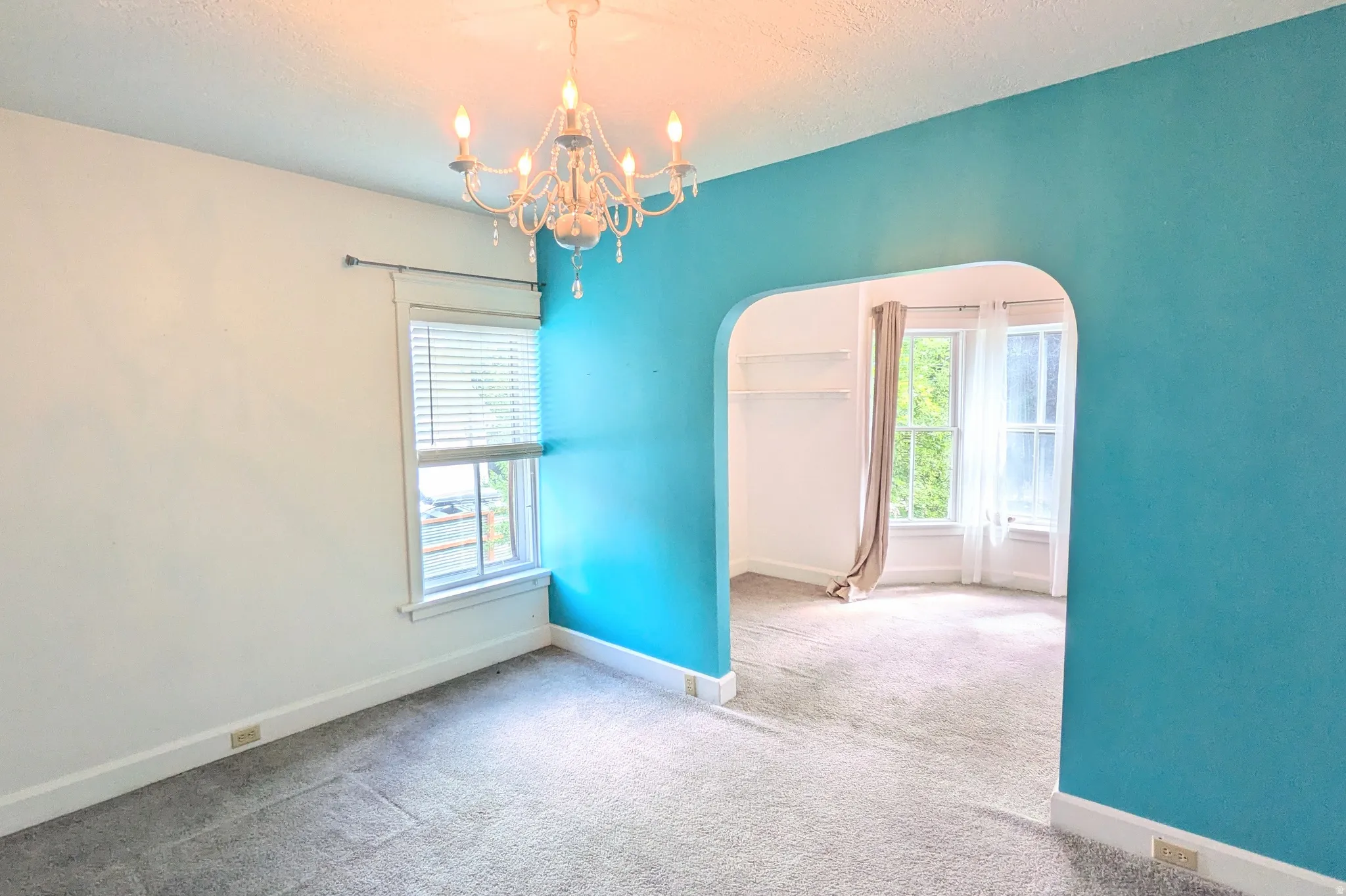 Arched doorway leading to an adjoining room, chandelier lighting, white trim, and light gray carpet