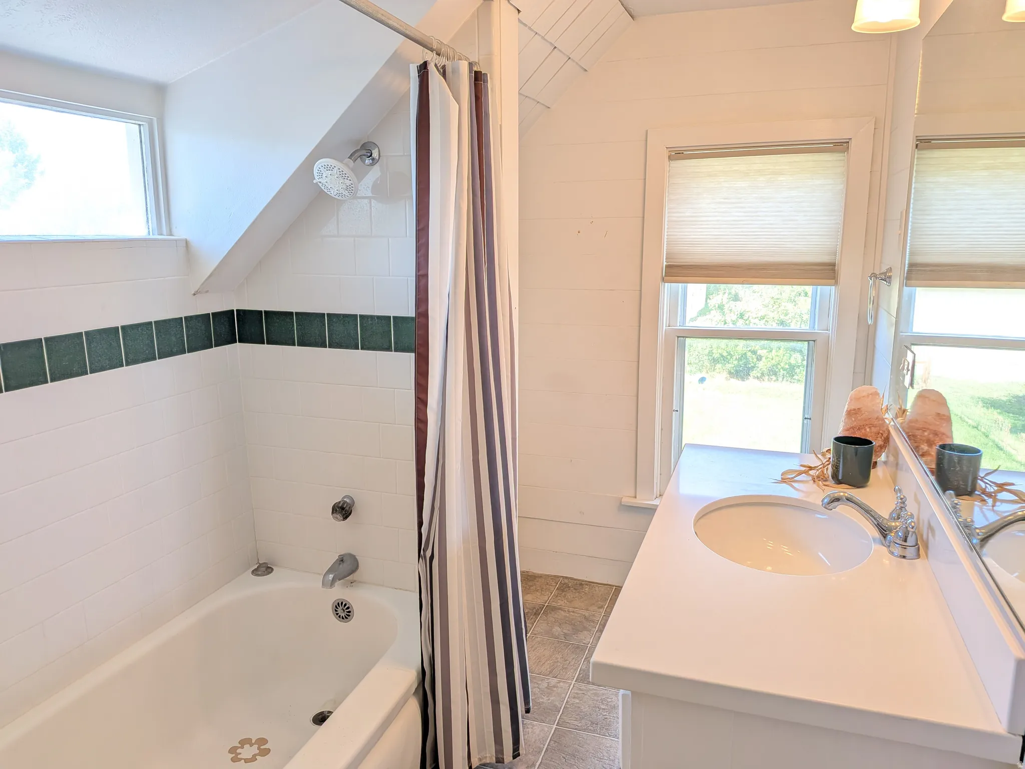 Bathroom featuring a white bathtub, ceramic tile surround with green accent, single vanity with integrated sink, and window with privacy shade