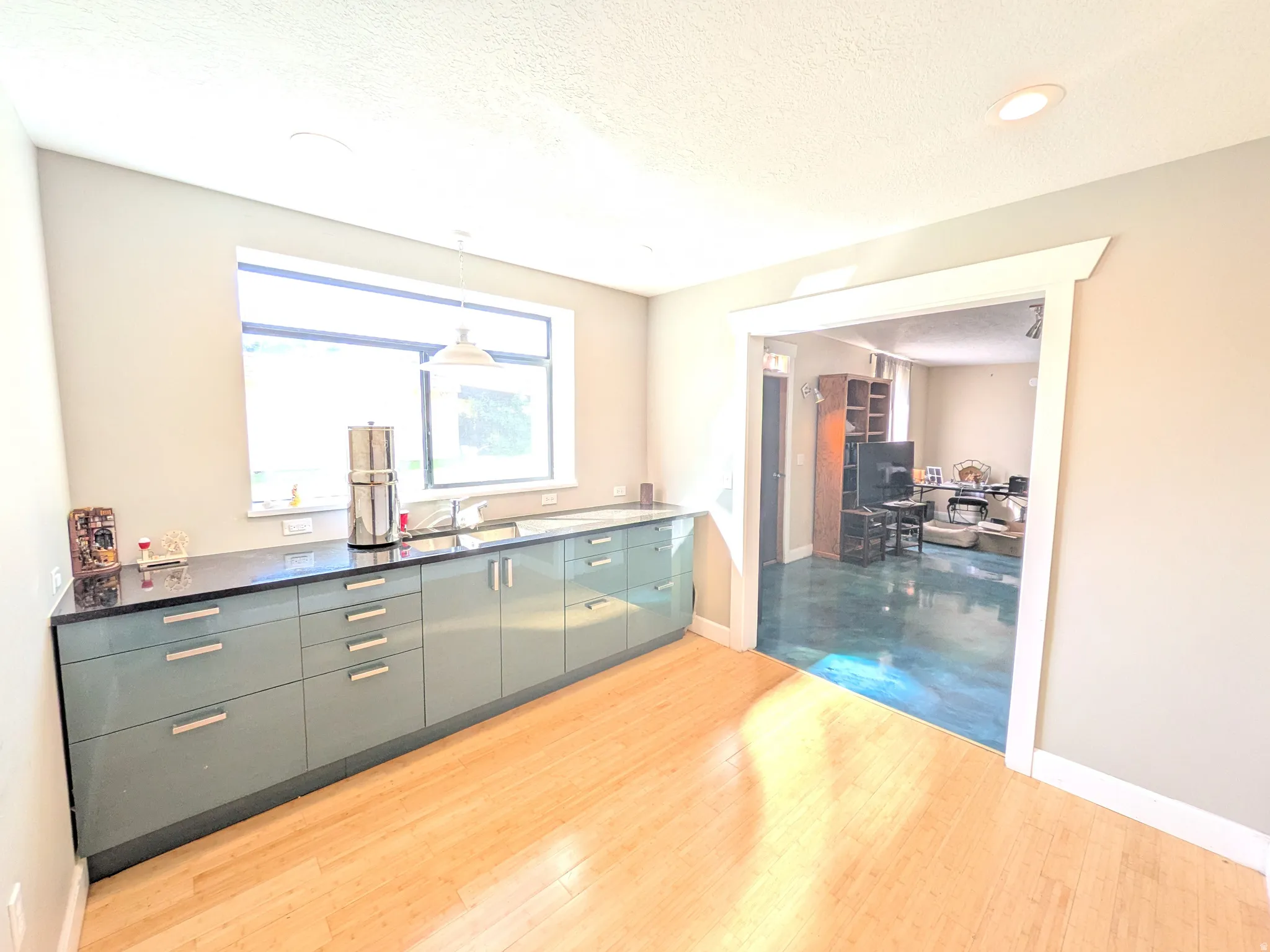 Wood-finish flooring, full-length counter with dark countertop, light blue cabinetry with brushed nickel hardware, and recessed lighting