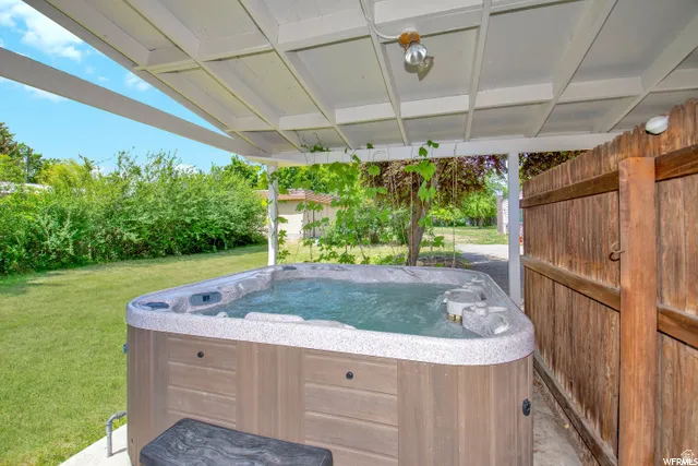 Outdoor spa with a wood-finish exterior, covered by a white pergola, set on a concrete pad