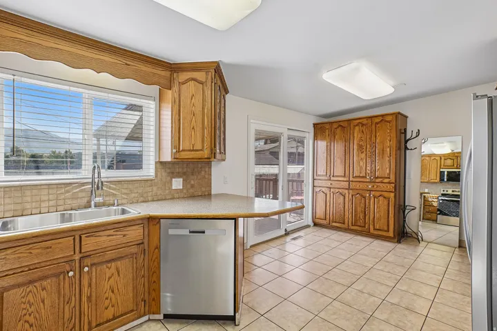 Wood-finish cabinetry, stainless steel dishwasher, tile flooring, sliding glass door, and built-in storage