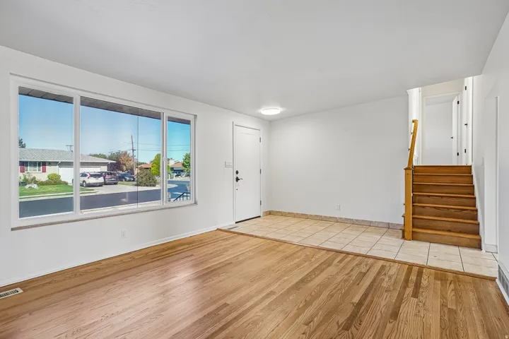Hardwood flooring, tiled entryway, white walls, large multi-pane window, and wooden staircase