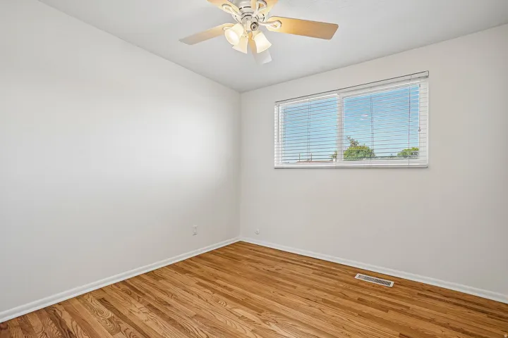 Hardwood-style flooring with white baseboards, bright white walls, and a ceiling-mounted fan with integrated lighting