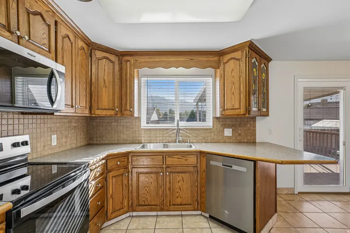 Kitchen featuring wood cabinetry, tiled backsplash, stainless steel appliances, and a built-in dishwasher