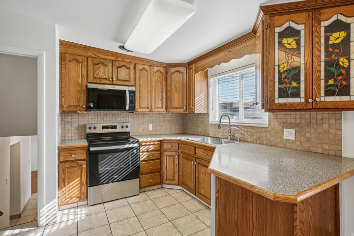 Kitchen featuring wood cabinetry, stainless steel appliances, mosaic tile backsplash, and composite countertops