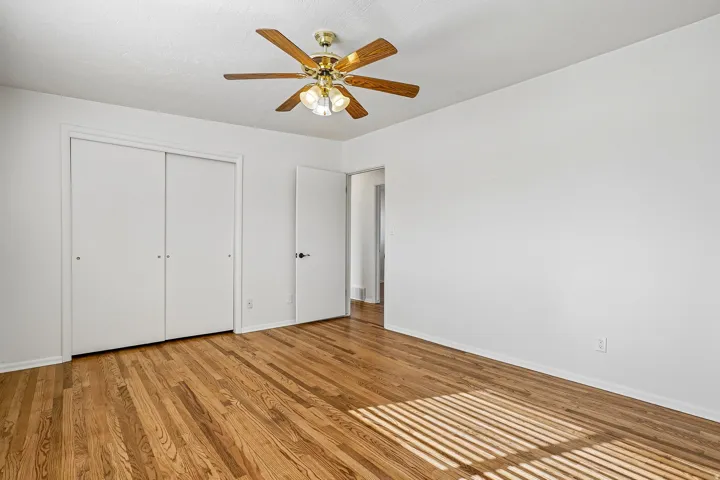 Hardwood flooring, white walls, ceiling fan with integrated lighting, sliding closet doors, and interior door