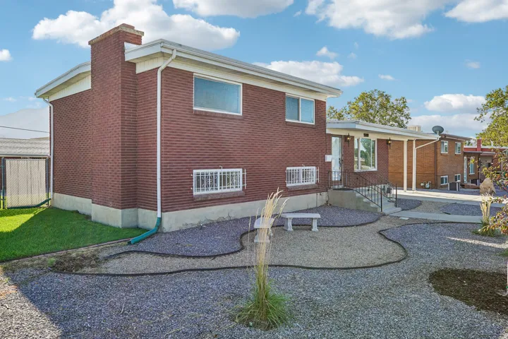 Brick exterior with a prominent chimney feature, an expansive gravel-covered yard, and a concrete paver path