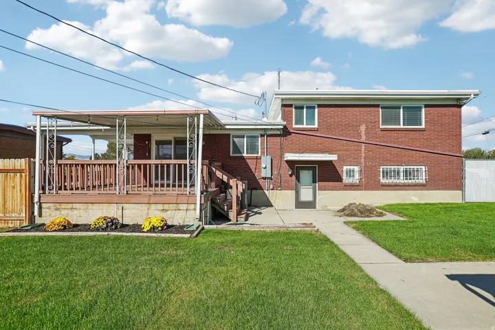 Brick exterior with a covered deck, wood deck railing, and concrete walkway
