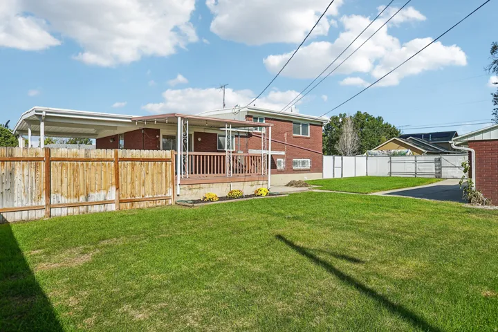 Expansive green lawn with a wooden privacy fence, a covered deck, and a carport