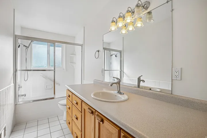 Bathroom featuring a wood vanity with integrated sink, a large mirror, and a shower-tub combination with sliding glass doors