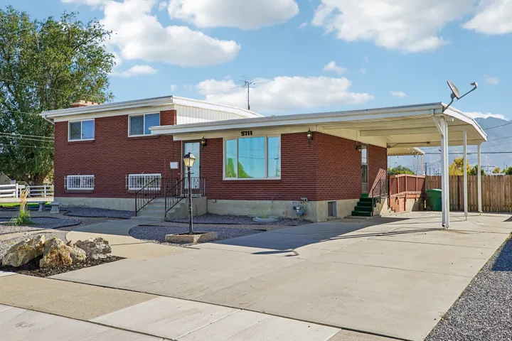 Brick exterior, covered carport, concrete driveway, front porch with wrought iron railings, and a streetlamp