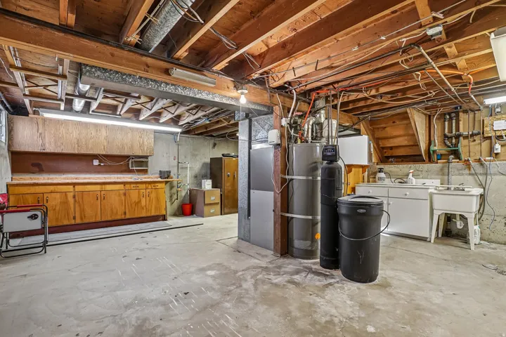 Unfinished basement featuring exposed wood joists, concrete flooring, a utility sink, and built-in wood cabinetry
