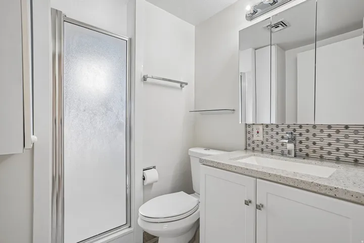 Shower with frosted glass door, white vanity with quartz countertop, under-mount sink, and mosaic tile backsplash