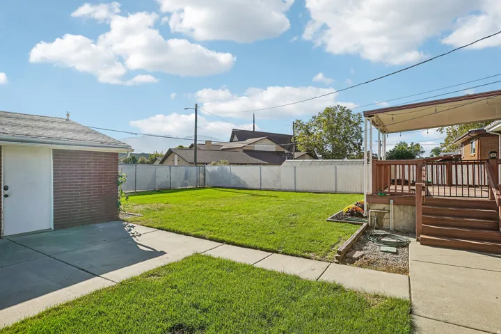 Expansive backyard featuring a manicured lawn, concrete patio, and a multi-level wood deck with a covered awning