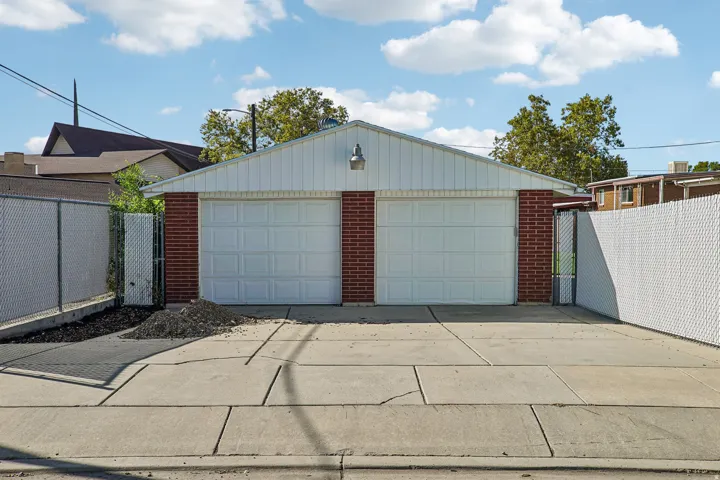 Two-car detached garage with brick accents and panel siding, featuring a concrete driveway and chain link fencing