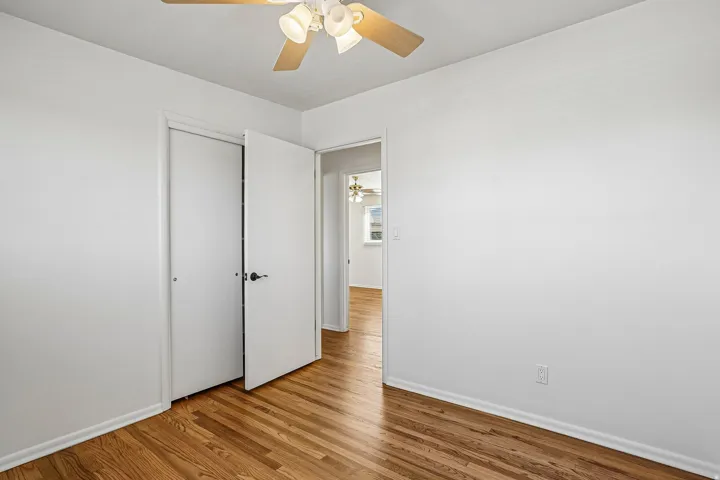 Wood-finish flooring, white walls, ceiling fan with light kit, and a closet with bifold doors