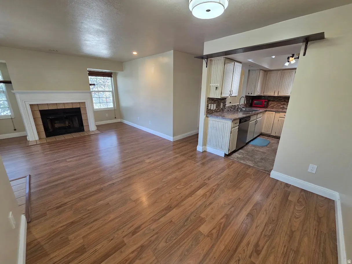 Wood-finish flooring throughout, living area with fireplace, and a kitchen featuring light cabinetry, a mosaic tile backsplash, and stainless steel appliances