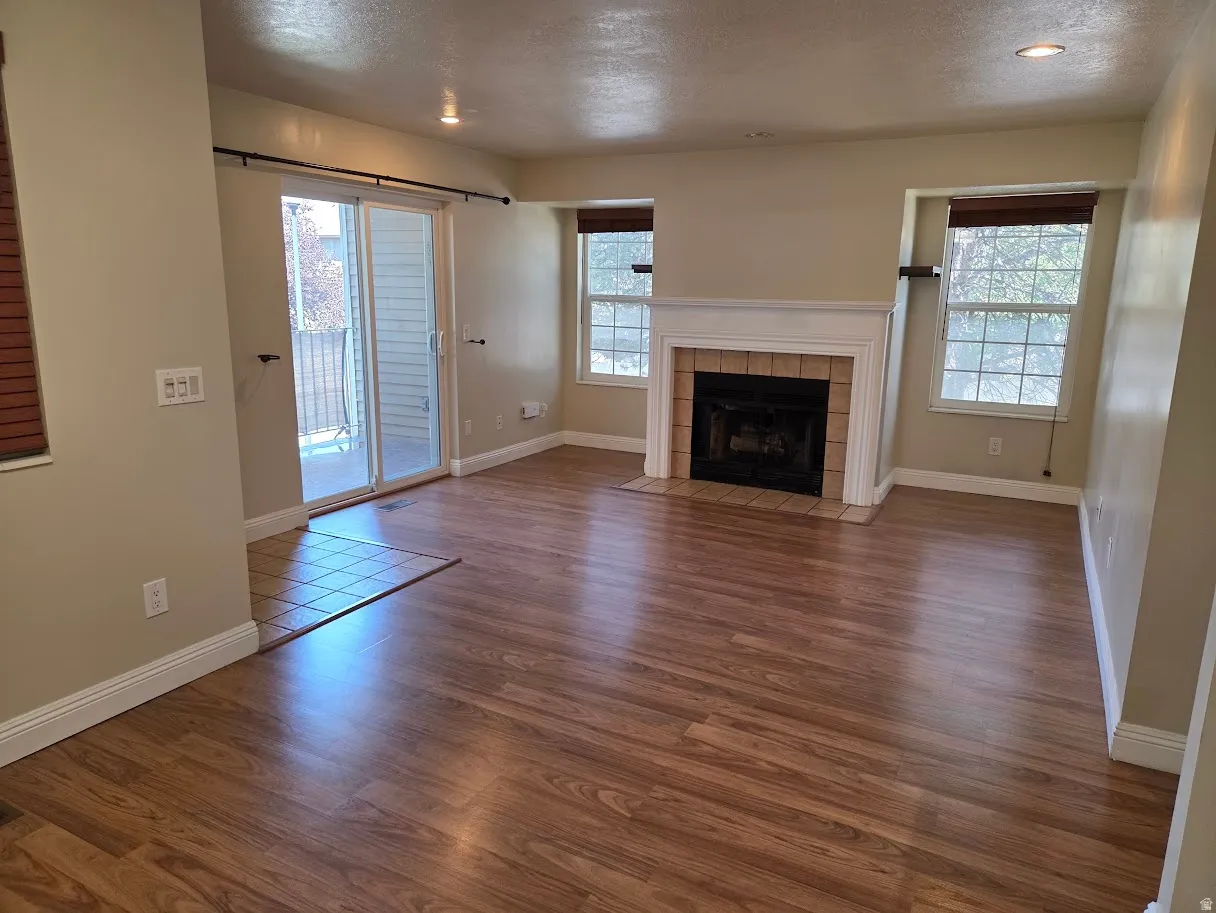 Living area featuring wood-finish flooring, a fireplace with a tile surround and white mantel, recessed lighting, and a glass sliding door providing access to an outdoor area