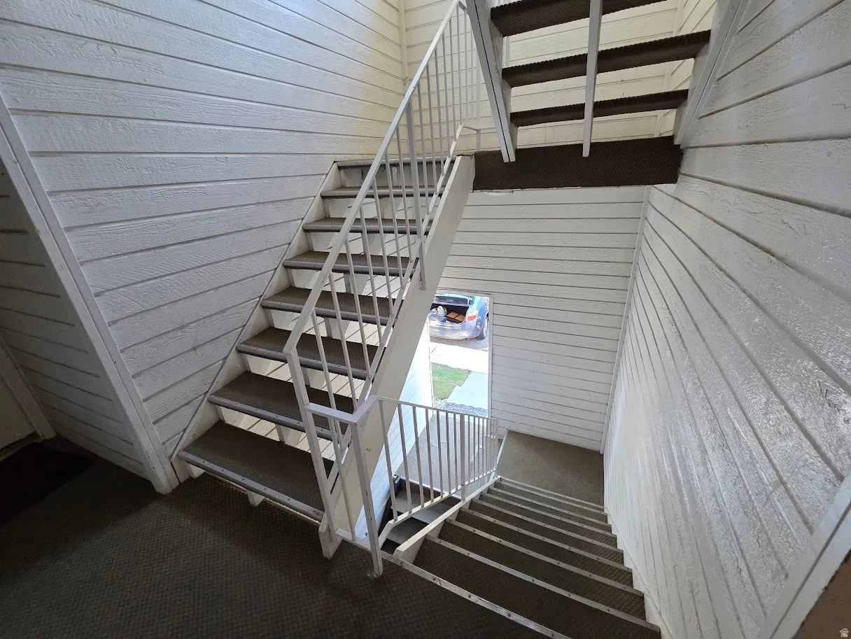 Multi-level staircase with white metal railings, textured wall paneling, and carpeted treads