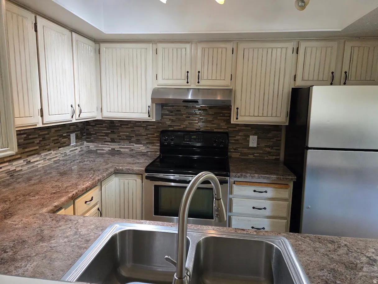Kitchen featuring an integrated double-basin sink with a stainless steel faucet, wood-finish countertops, tile backsplash, and beadboard-style cabinetry with dark hardware