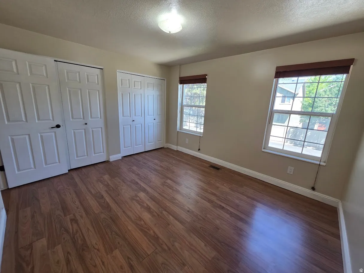 Primary bedroom with Wood-finish flooring throughout, featuring two windows with blinds, and two sets of bi-fold closet doors