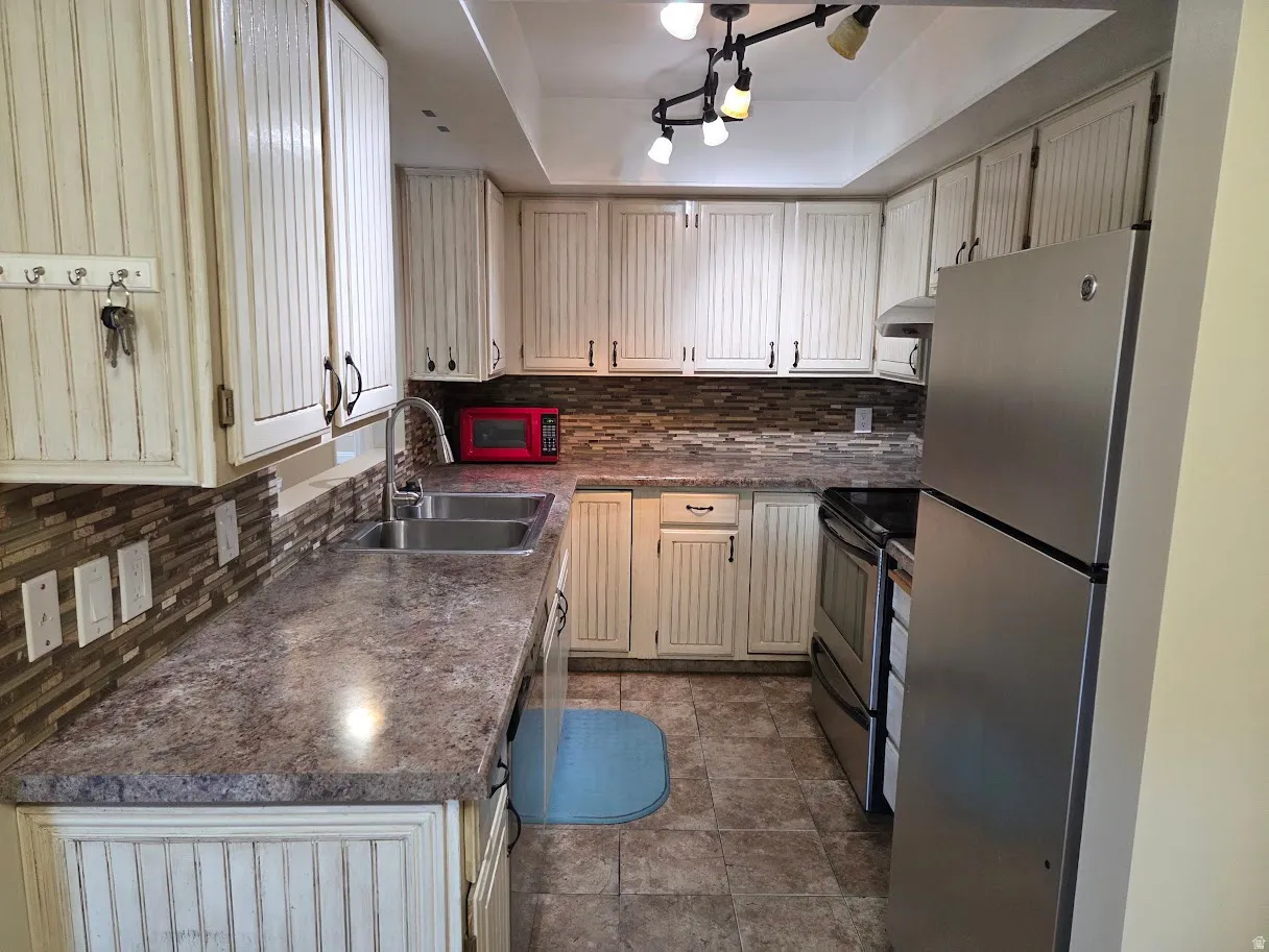 Kitchen featuring white beadboard cabinetry, stainless steel appliances, dual basin sink, tiled flooring, and a tile backsplash