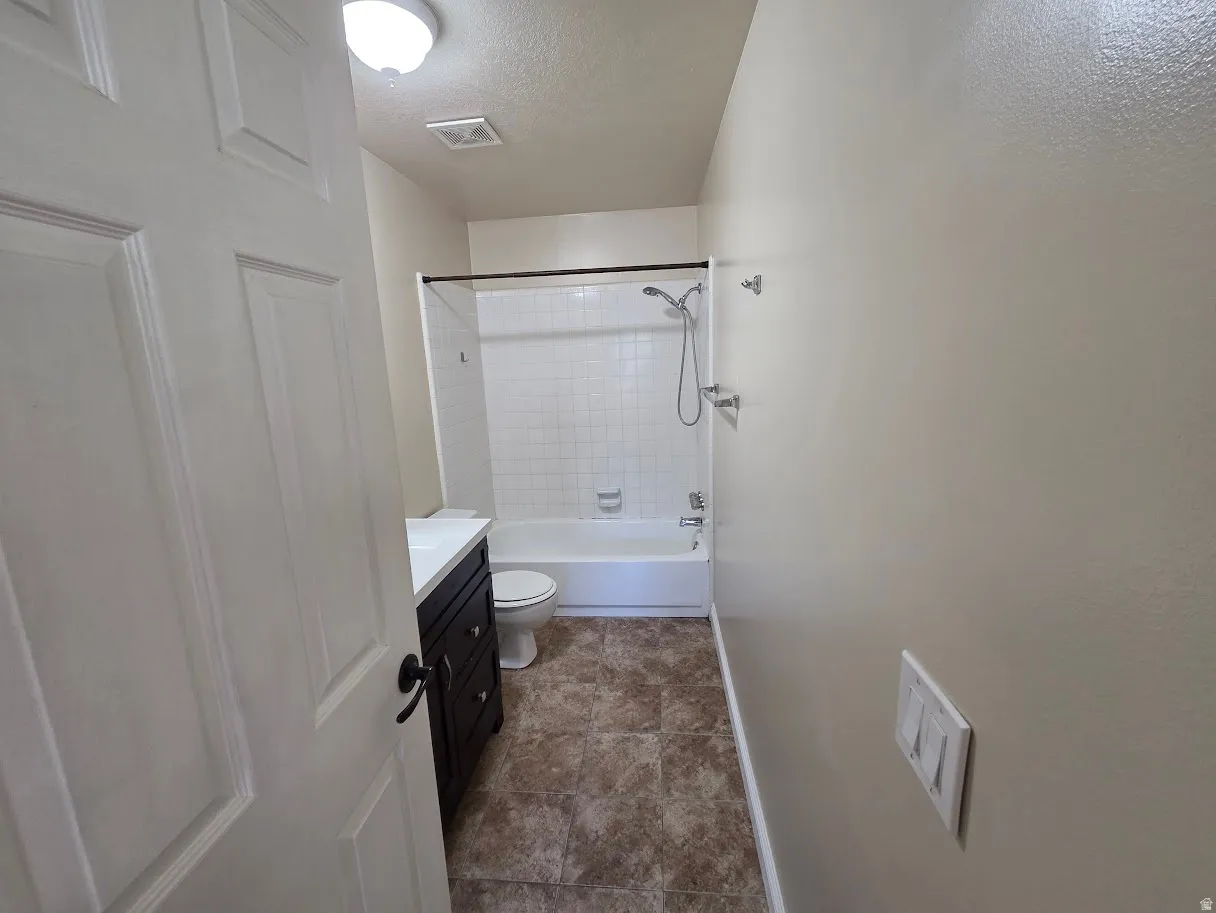 Full Primary Bathroom featuring a dark wood-finish vanity with a white countertop, a white toilet, and a white tiled shower/tub combination