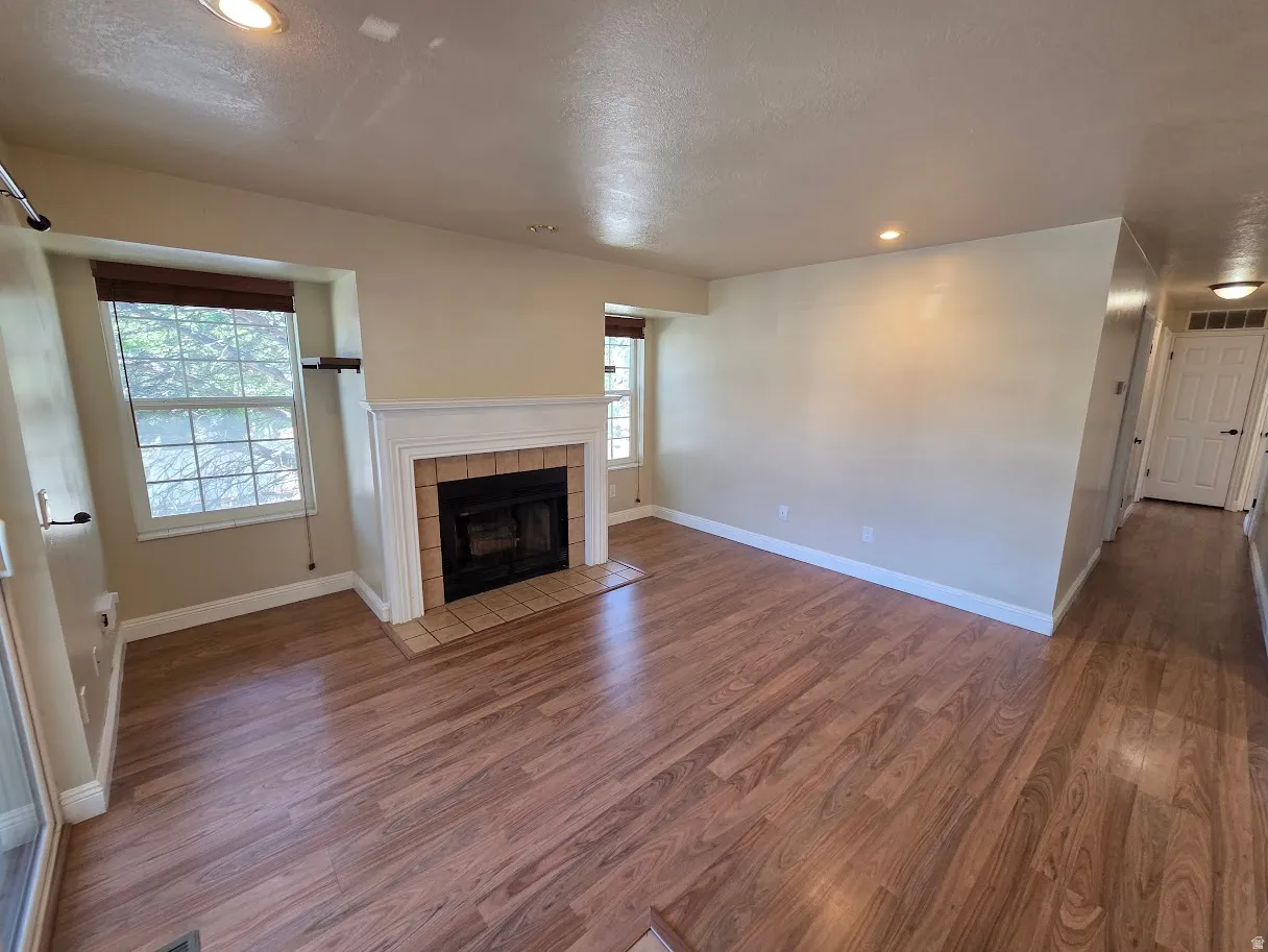 Wood-finish flooring throughout, fireplace with tile surround and mantel, recessed lighting, and multiple windows with blinds