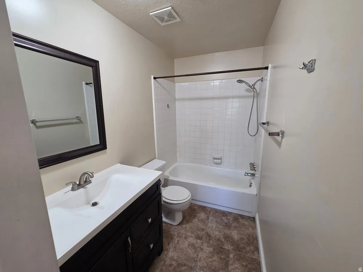 Primary Bathroom featuring a dark wood vanity with an integrated white sink, a framed mirror, a tiled shower/tub combination, and textured floor tiling