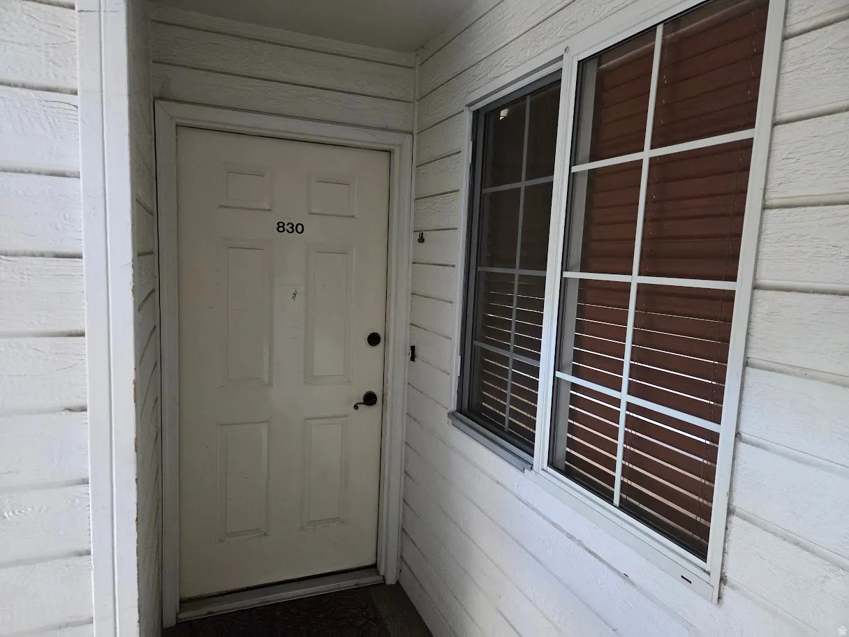 White paneled door with dark hardware, accompanied by a window featuring blinds and a grid pattern, set against horizontal siding