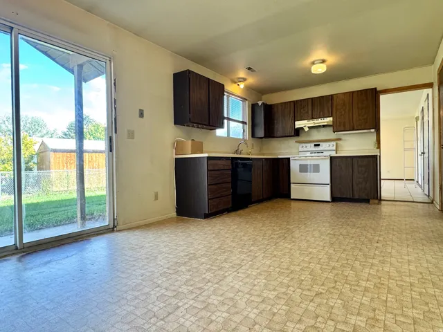 Unit 1 Kitchen featuring wood-finish cabinetry, white stove, and sliding glass door access to the backyard. Doorway to 2nd Kitchen on the right.