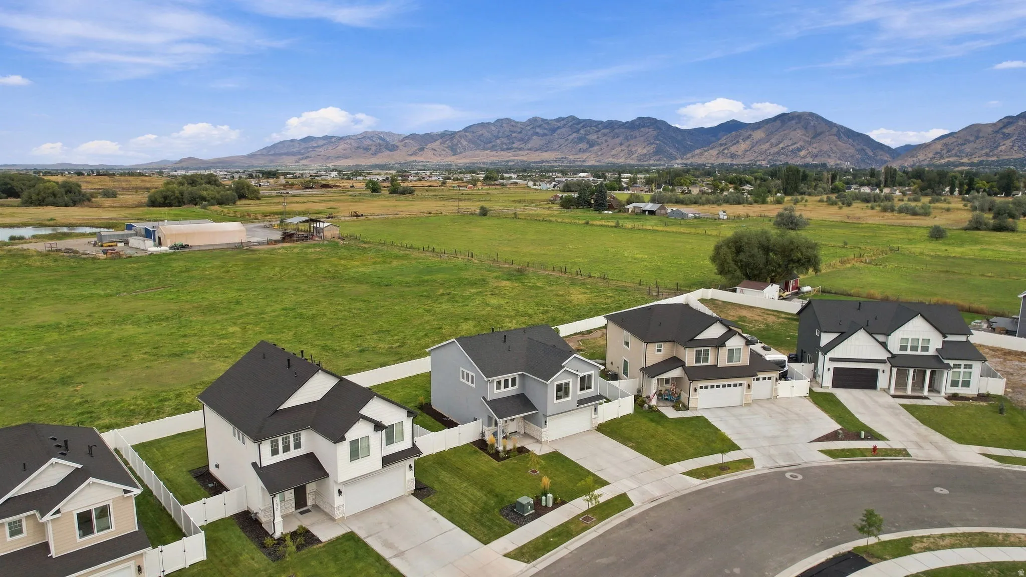 New construction homes with varied exterior finishes, concrete driveways, and manicured lawns, set against a backdrop of distant mountains