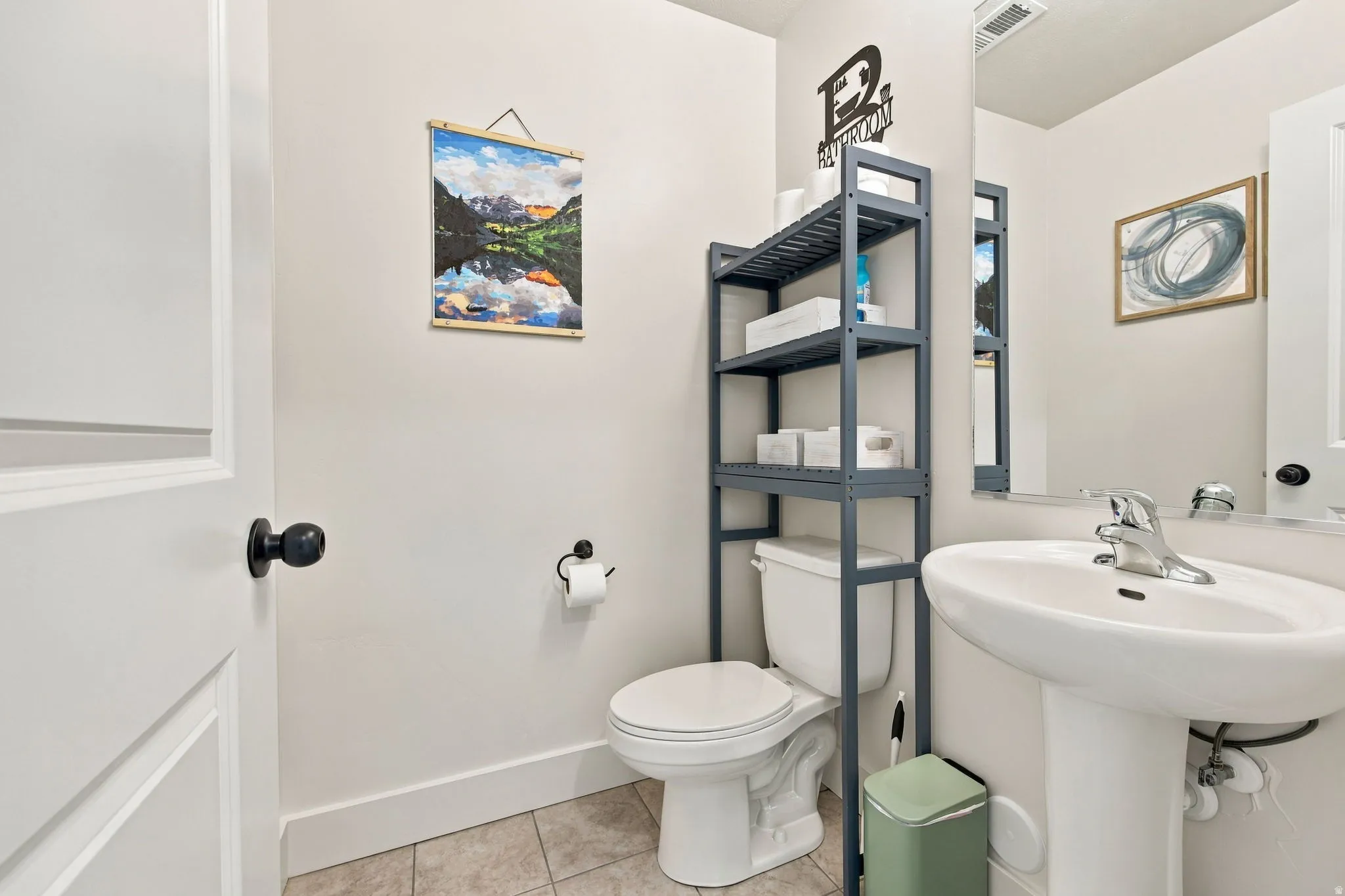 Pedestal sink with chrome faucet, white paneled door with black hardware, and an integrated toilet with shelving