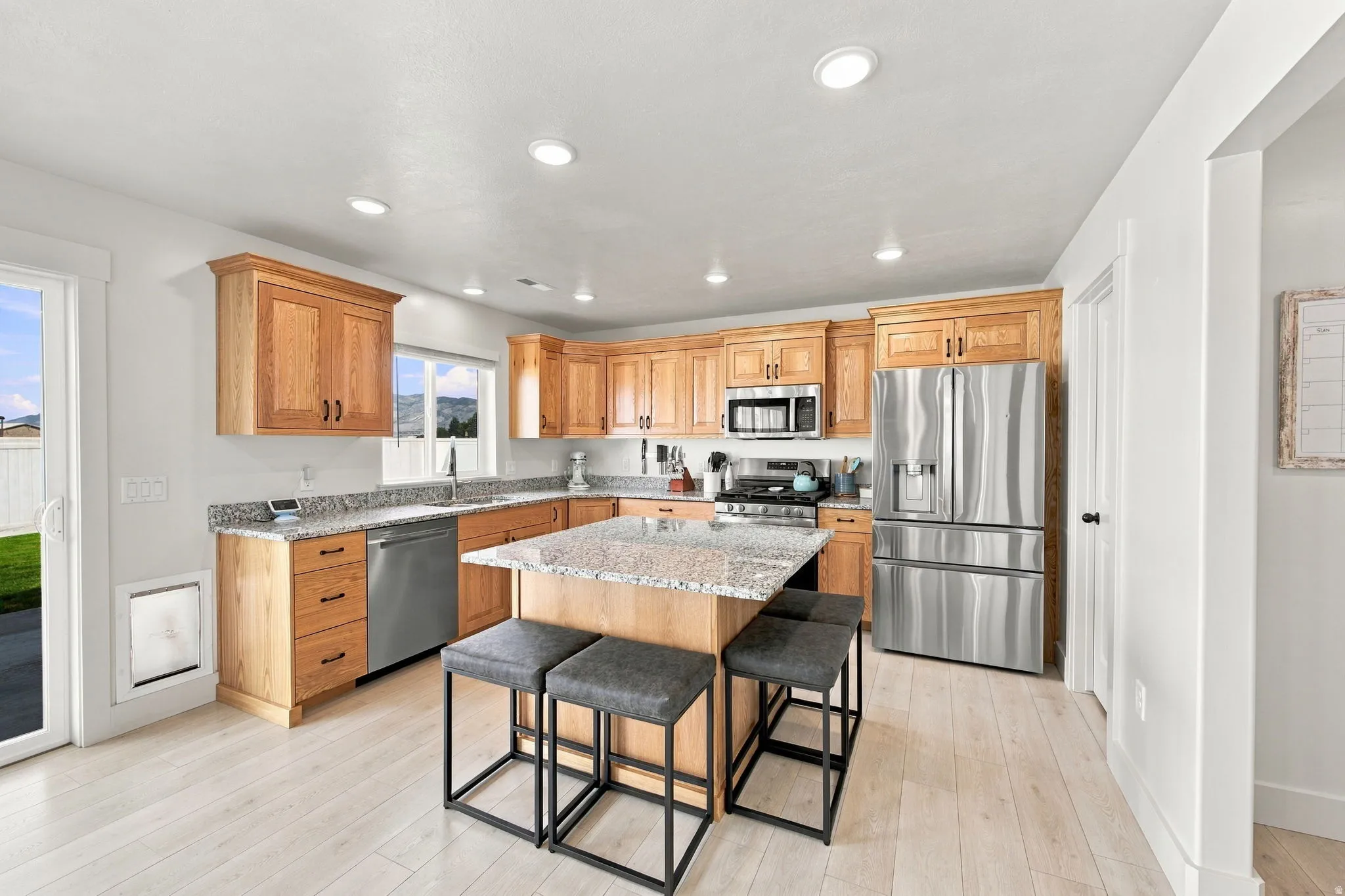 Kitchen featuring a central island, light wood cabinetry, granite countertops, stainless steel appliances, and light wood-finish flooring