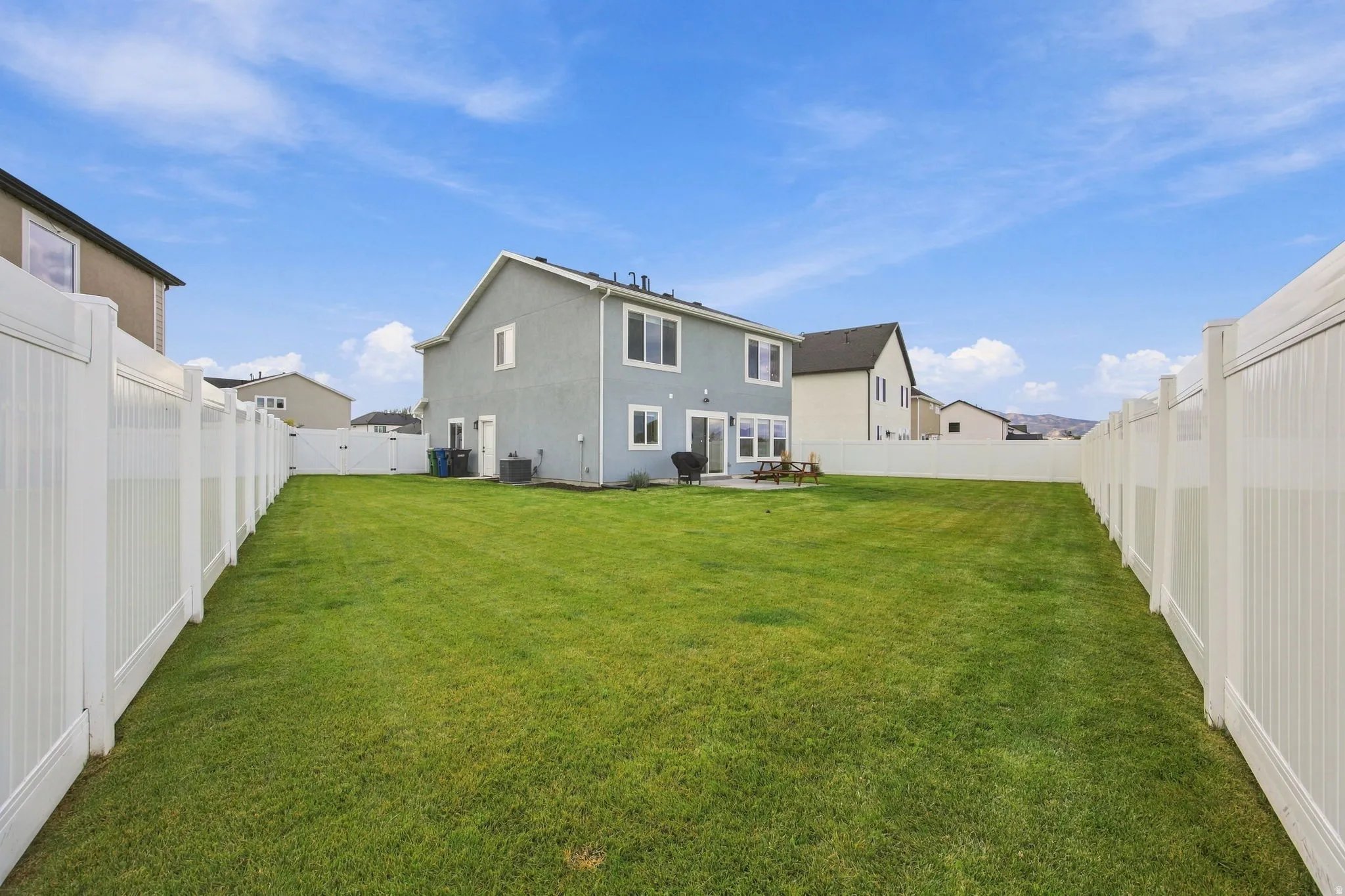 Expansive backyard featuring a manicured lawn, white vinyl fencing, and a concrete patio
