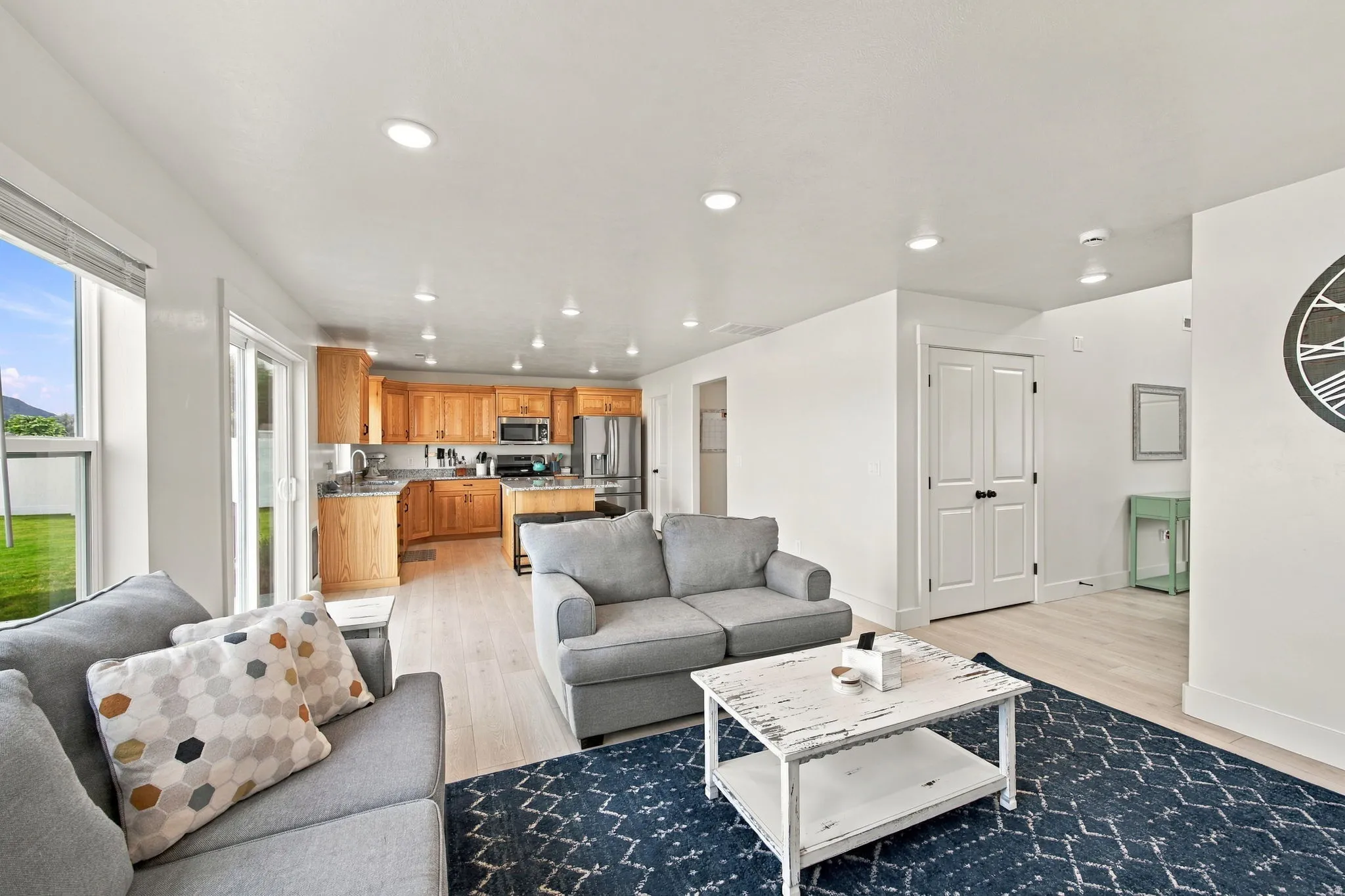 Open-concept living area with light-toned wood-finish flooring, recessed lighting, and a sliding glass door leading to the exterior