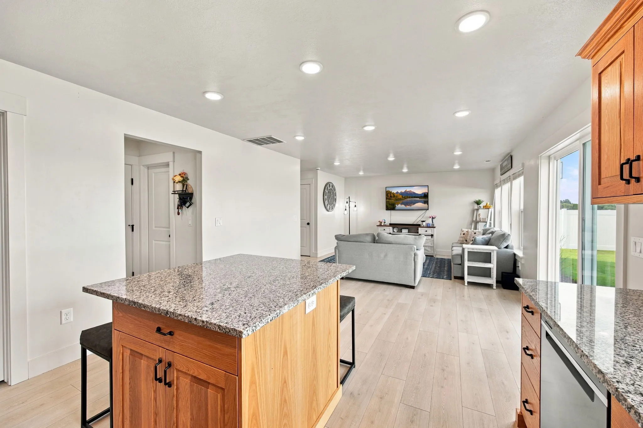 Kitchen island with granite countertop and wood cabinetry, light wood-finish flooring, recessed lighting, white walls, and a sliding glass door to the exterior