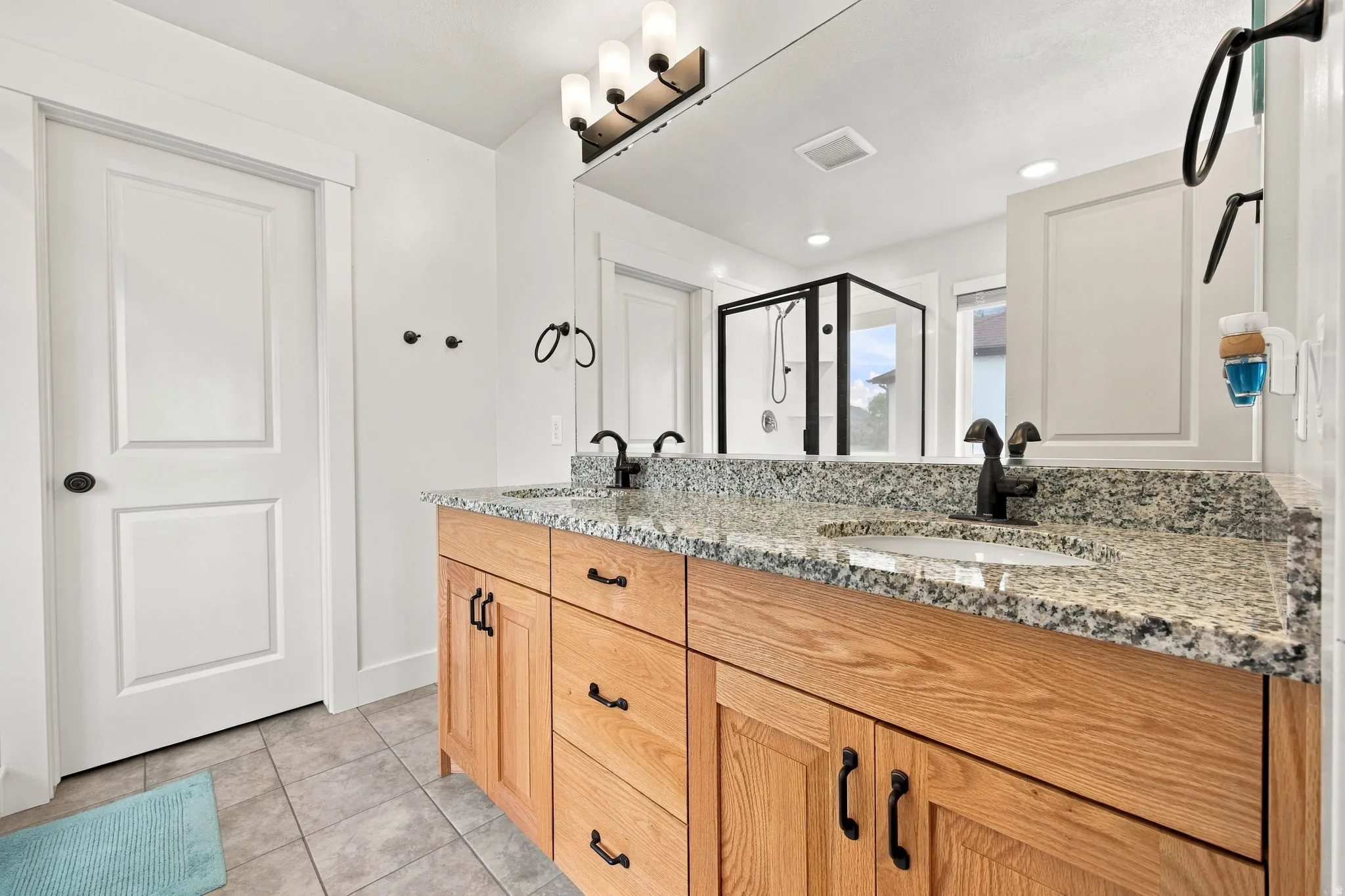 Dual sink vanity with granite countertop, wood-finish cabinetry, and matte black fixtures