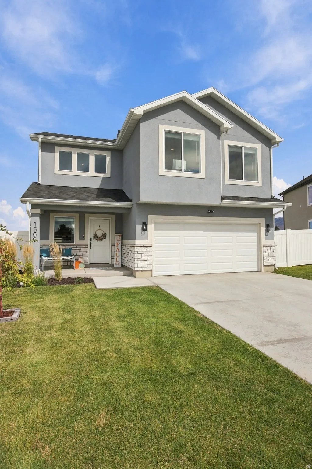 Two-story stucco exterior with stone accents, black roof, attached garage, and a concrete driveway