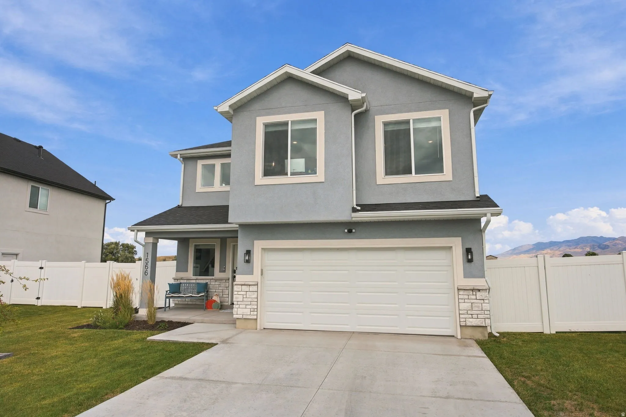 Two-story stucco exterior featuring a two-car garage, covered entry, and white vinyl fencing
