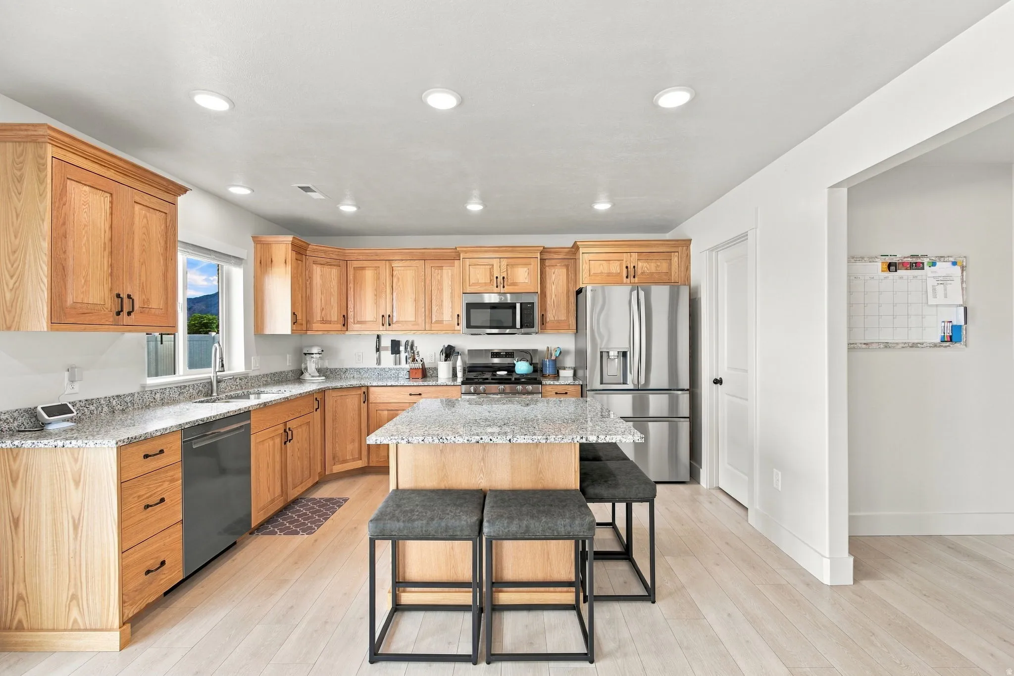 Kitchen featuring wood cabinetry, light-colored wood-finish flooring, recessed lighting, stainless steel appliances, and a central island with a light-toned countertop