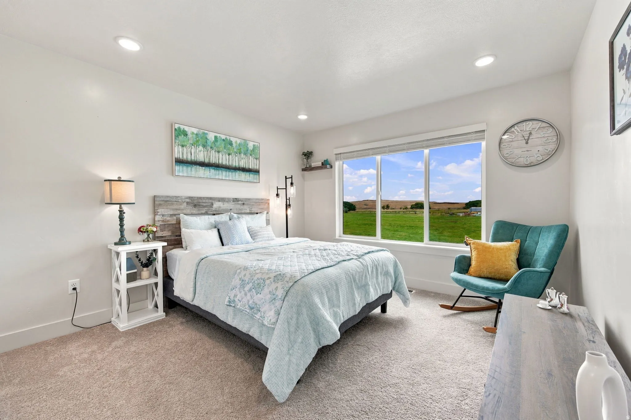 Recessed lighting, wood-finish headboard, window with exterior scenery, wall-to-wall carpeting, and bright white walls