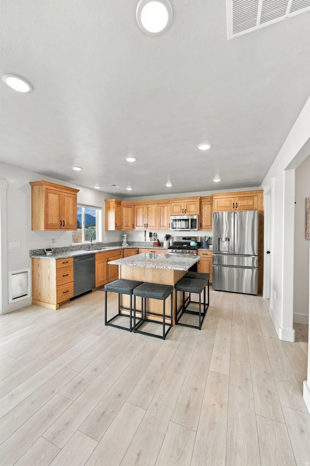 Kitchen featuring wood-finish flooring, recessed lighting, wood cabinetry, stone countertops, and a center island with seating
