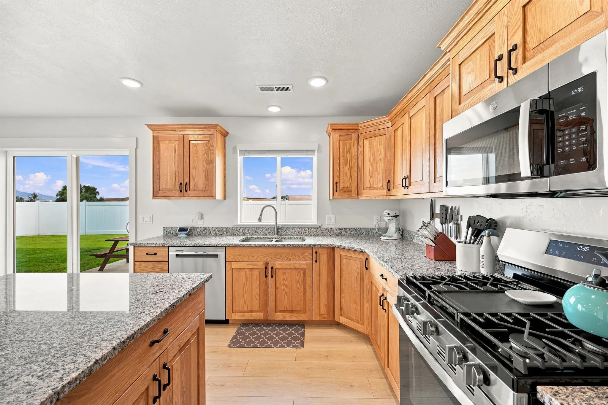 Kitchen featuring light wood cabinetry, stone countertops, stainless steel appliances, and wood-finish flooring