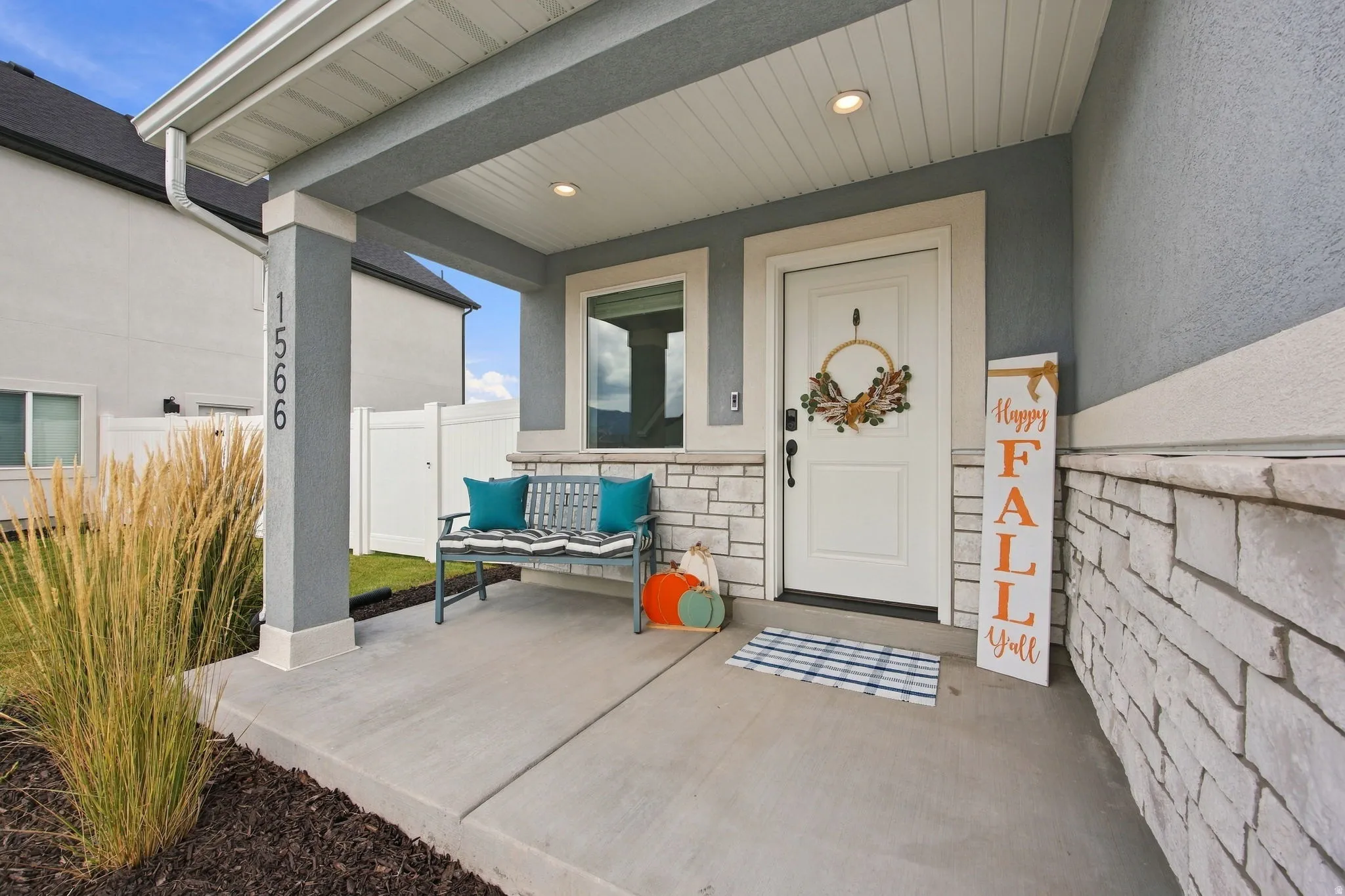 Covered concrete porch with recessed lighting, stone veneer accents, and a white entry door