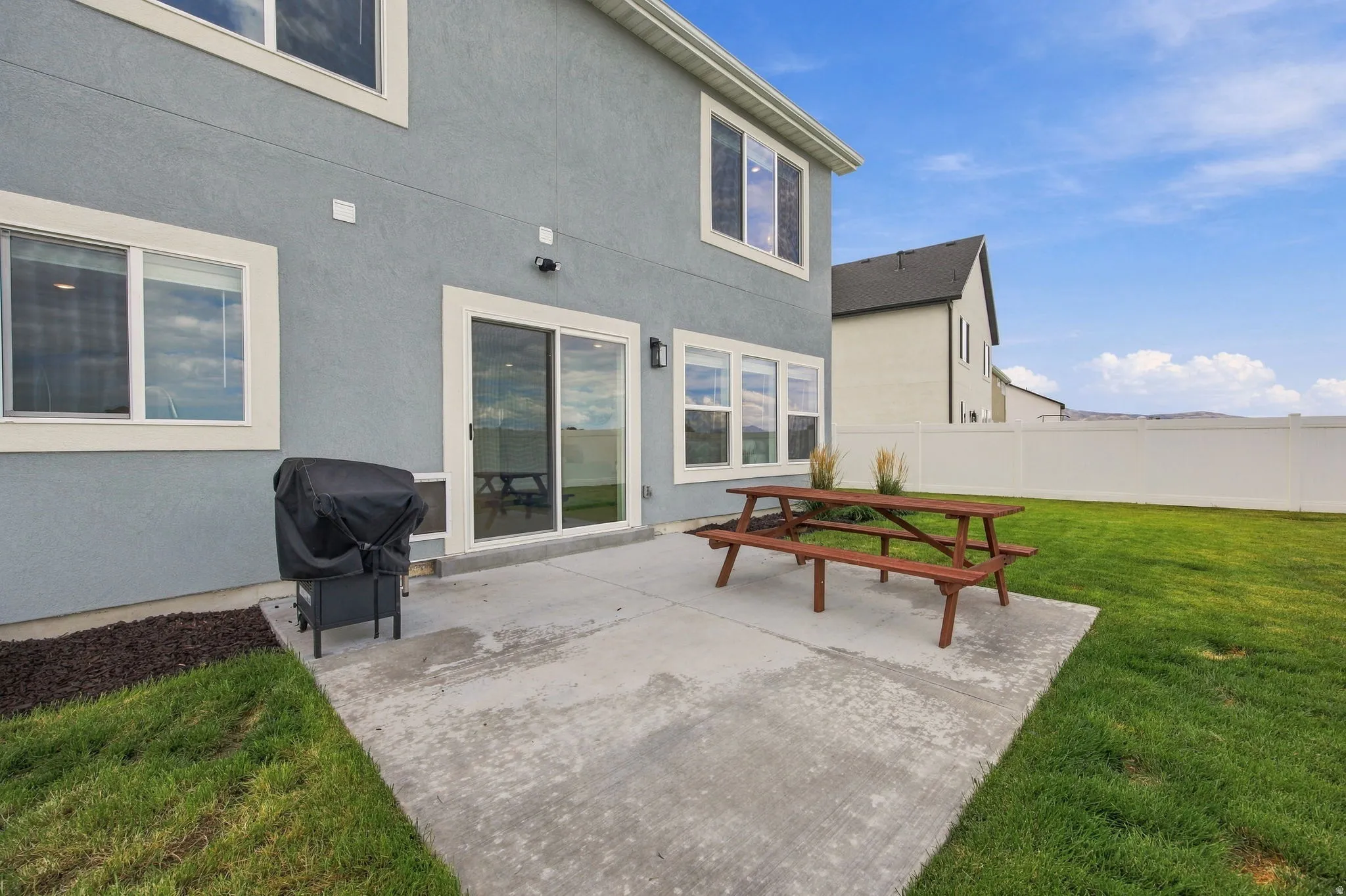 Rear exterior with a concrete patio, sliding glass door, and multiple windows