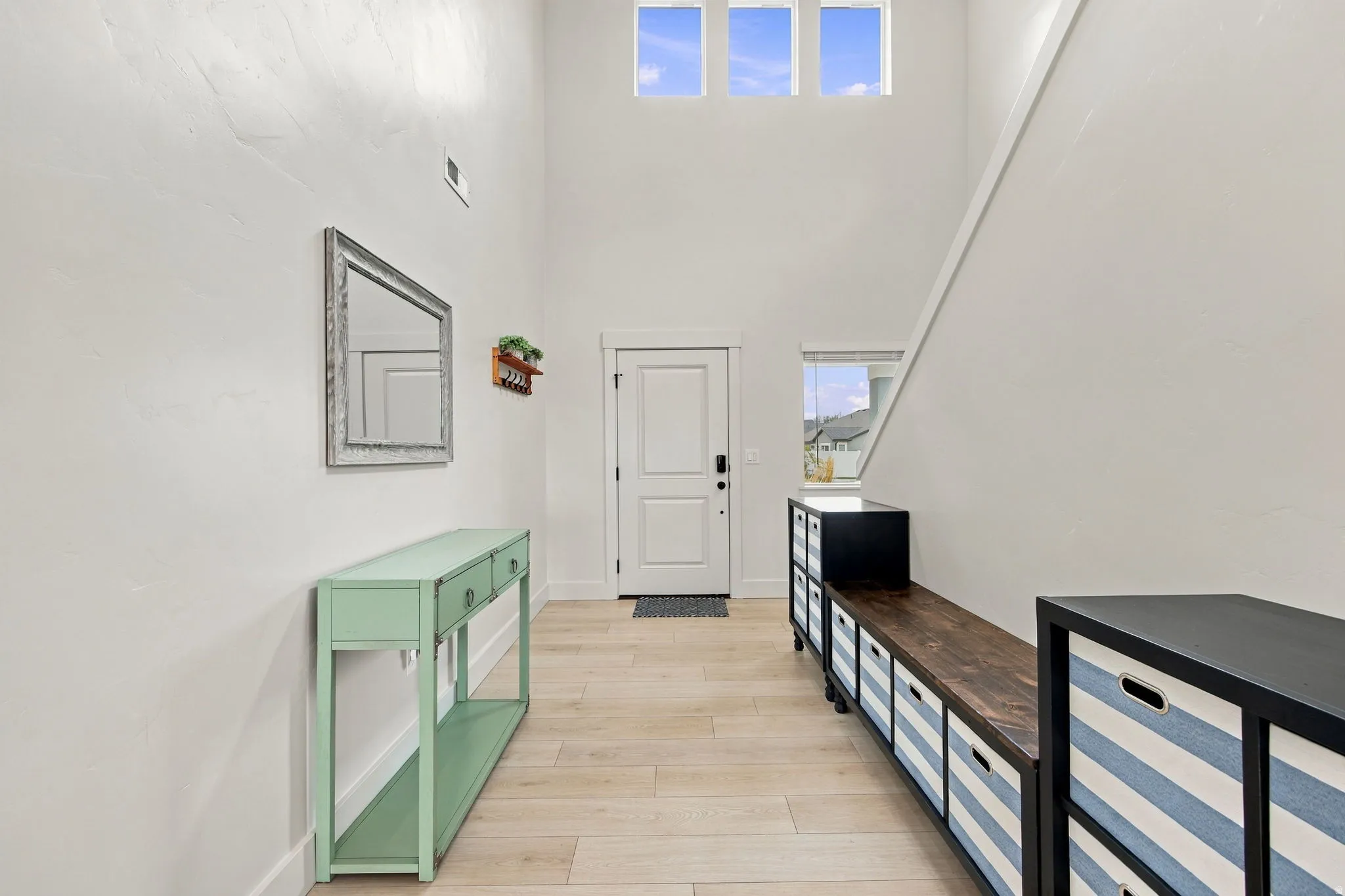 Vaulted entry with abundant natural light, light wood-finish flooring, and white interior walls