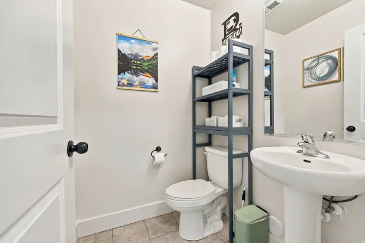 Pedestal sink with chrome faucet, white paneled door with black hardware, and an integrated toilet with shelving