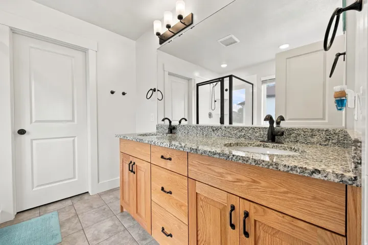 Dual sink vanity with granite countertop, wood-finish cabinetry, and matte black fixtures