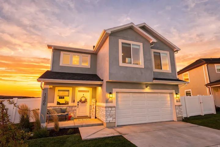 Two-story stucco exterior with stone accents, covered front porch, white garage door, and well-maintained landscaping